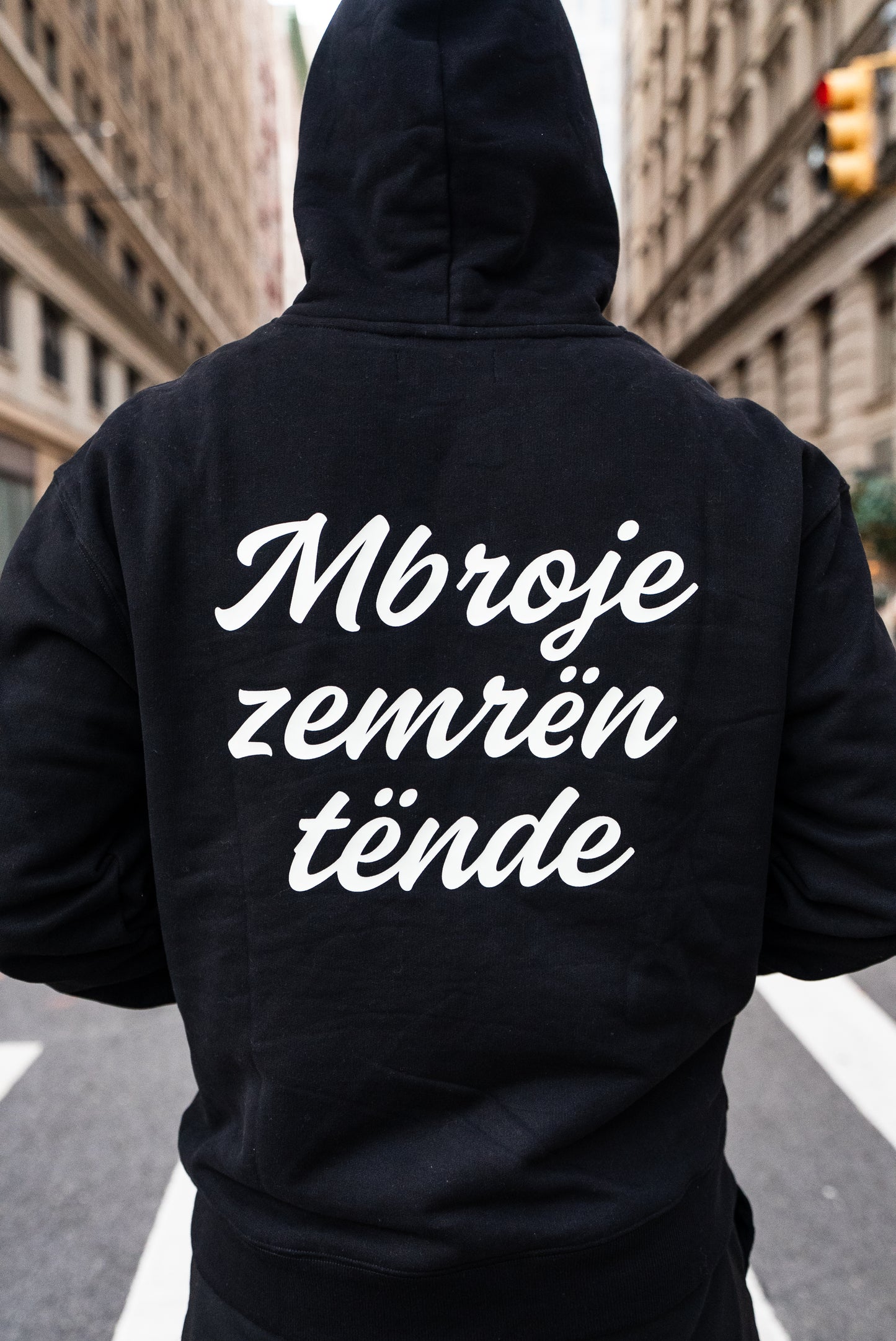 Person wearing a black hoodie with text on the back in an urban setting