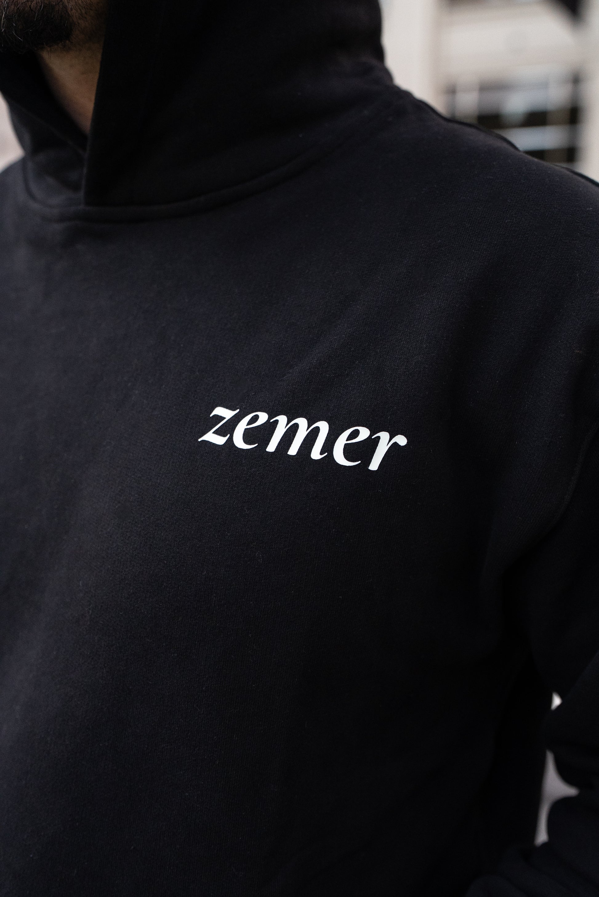 Black hoodie with 'zemer' logo on a blurred background