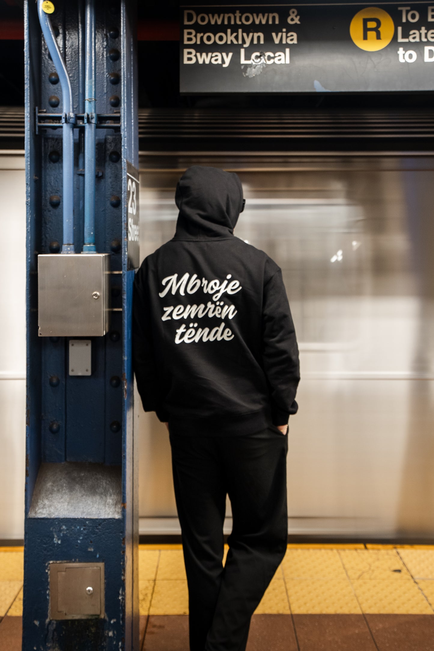 Person wearing a black hoodie with text in a subway station