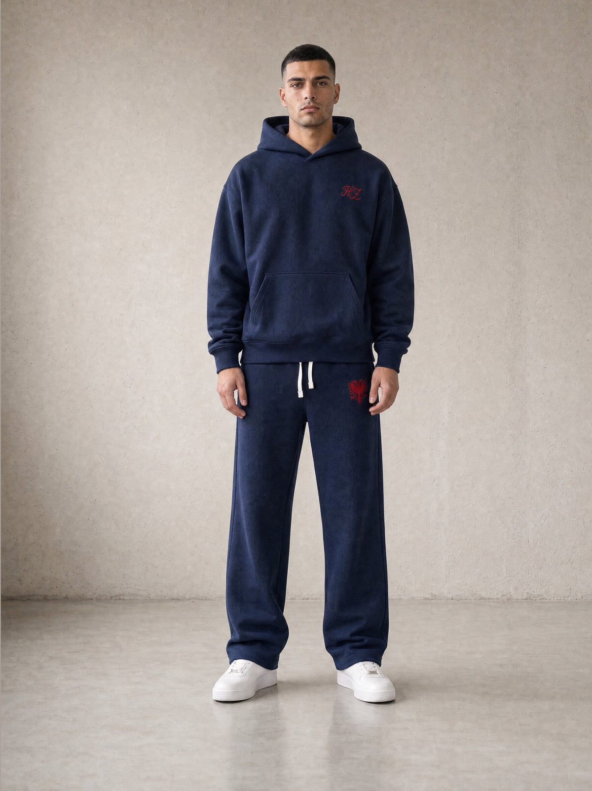 Design preview: Hajde Zemer HZ Essential Eagle Set in blue navy, front view on a male model, red eagle on the sweatpant thigh