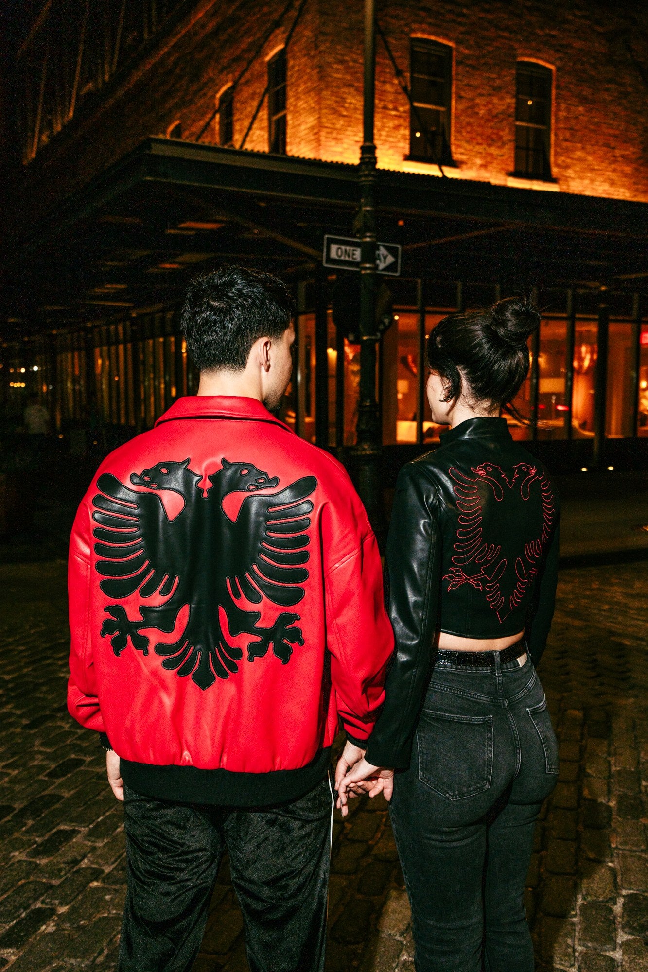 Couple wearing Albanian Red and Black Eagle Jackets on a city street at night