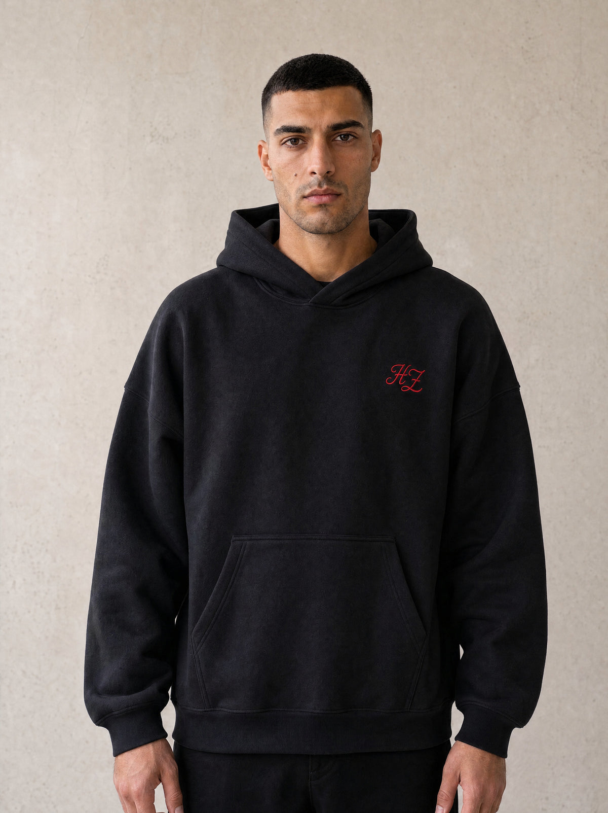 Man wearing the black Hajde Zemer Essential Eagle hoodie, front view, red HZ chest mark visible