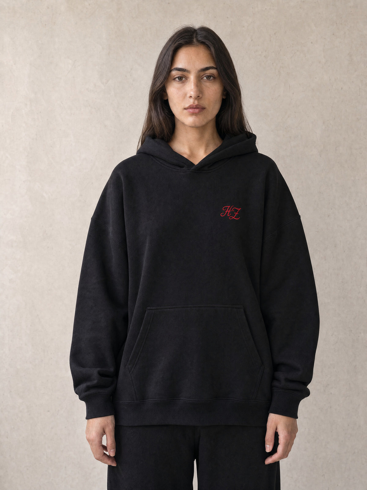 Woman wearing the black Hajde Zemer Essential Eagle hoodie, front view, red HZ chest mark visible