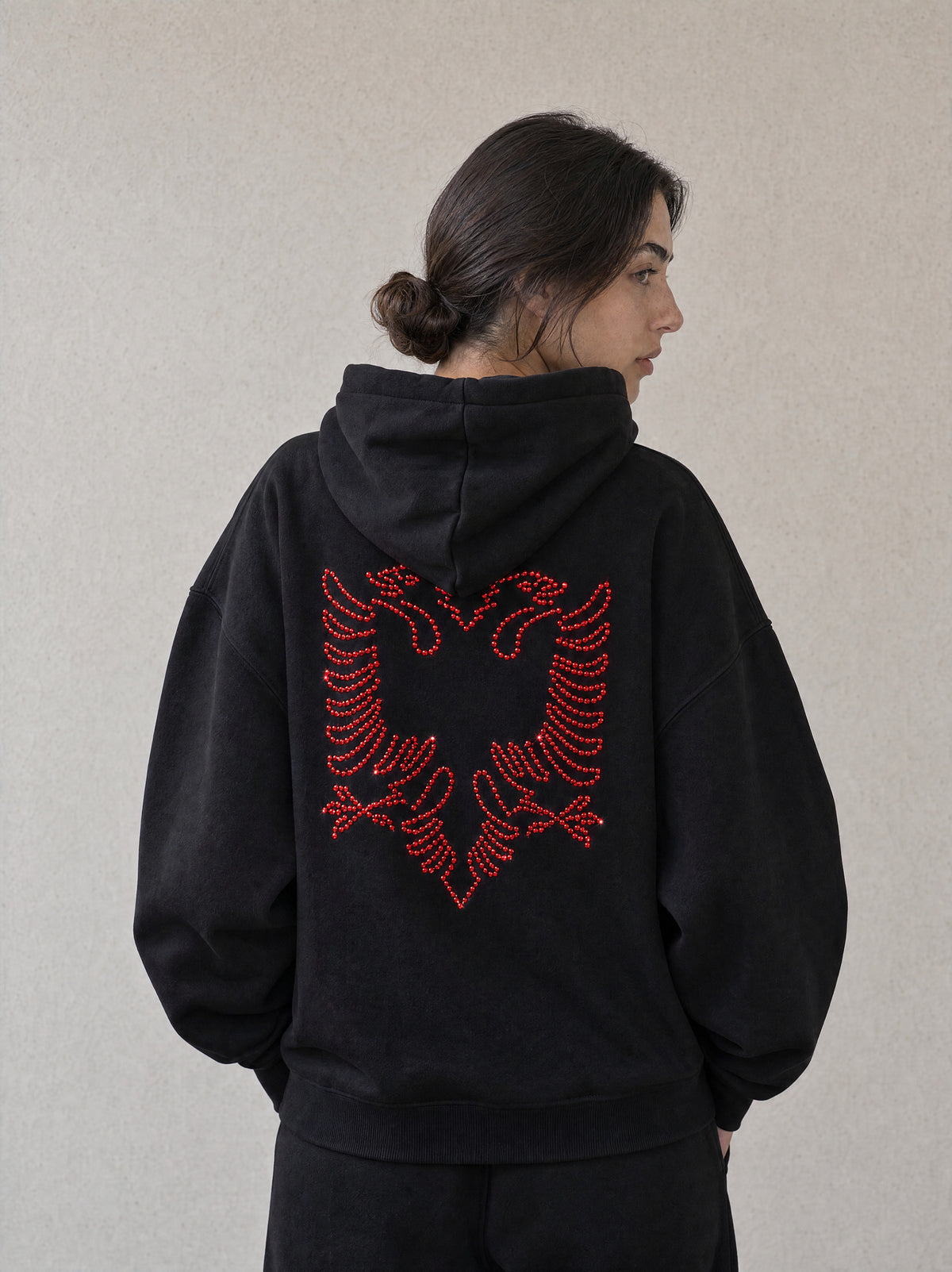 Woman wearing the black Hajde Zemer Essential Eagle hoodie, back view, red outline Albanian eagle across the back