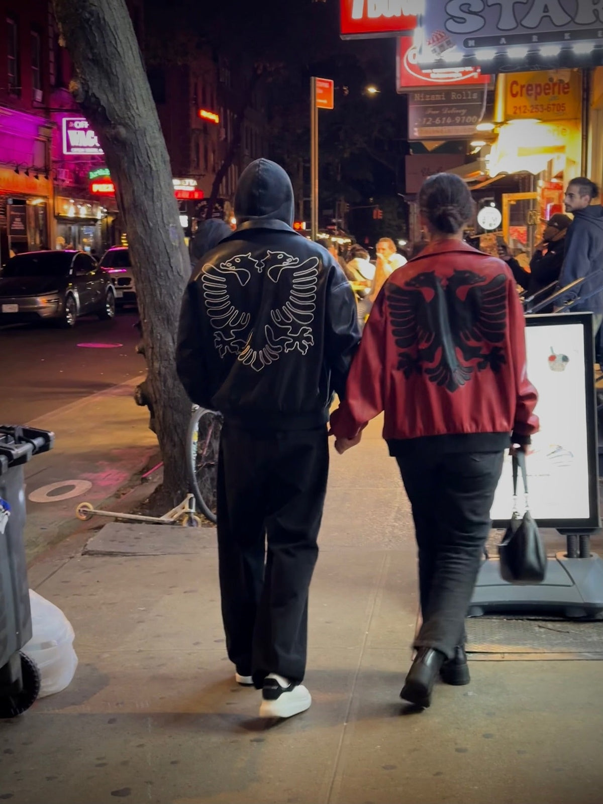 Couple wearing Albanian Eagle Jackets walking NYC streets at night — black and red eagle jackets paired together | Hajde Zemer