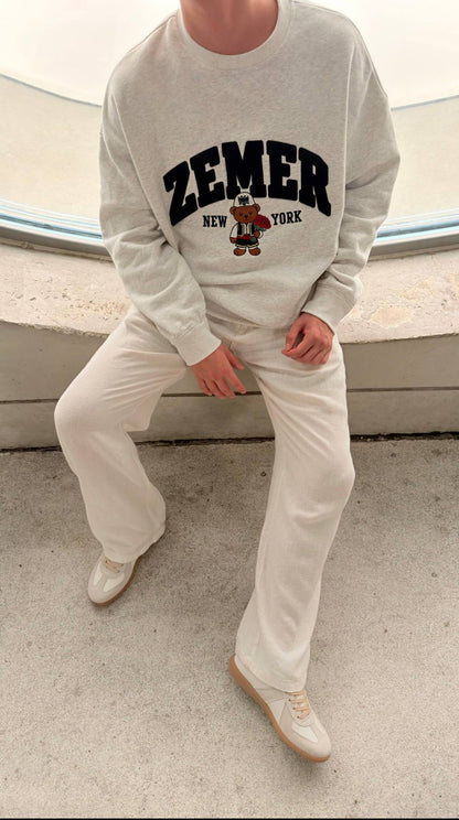 ZEMER Bear Crewneck in heather grey, worn seated with cream trousers, ZEMER New York be, on the ZEMER Bear Crewneck - Kids page