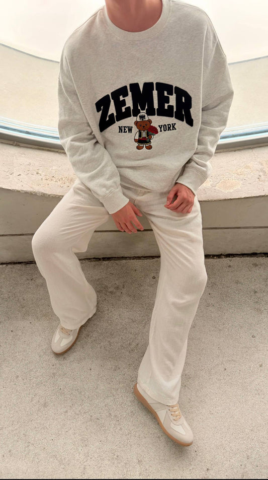ZEMER Bear Crewneck worn with cream trousers, seated, showing the full relaxed cut