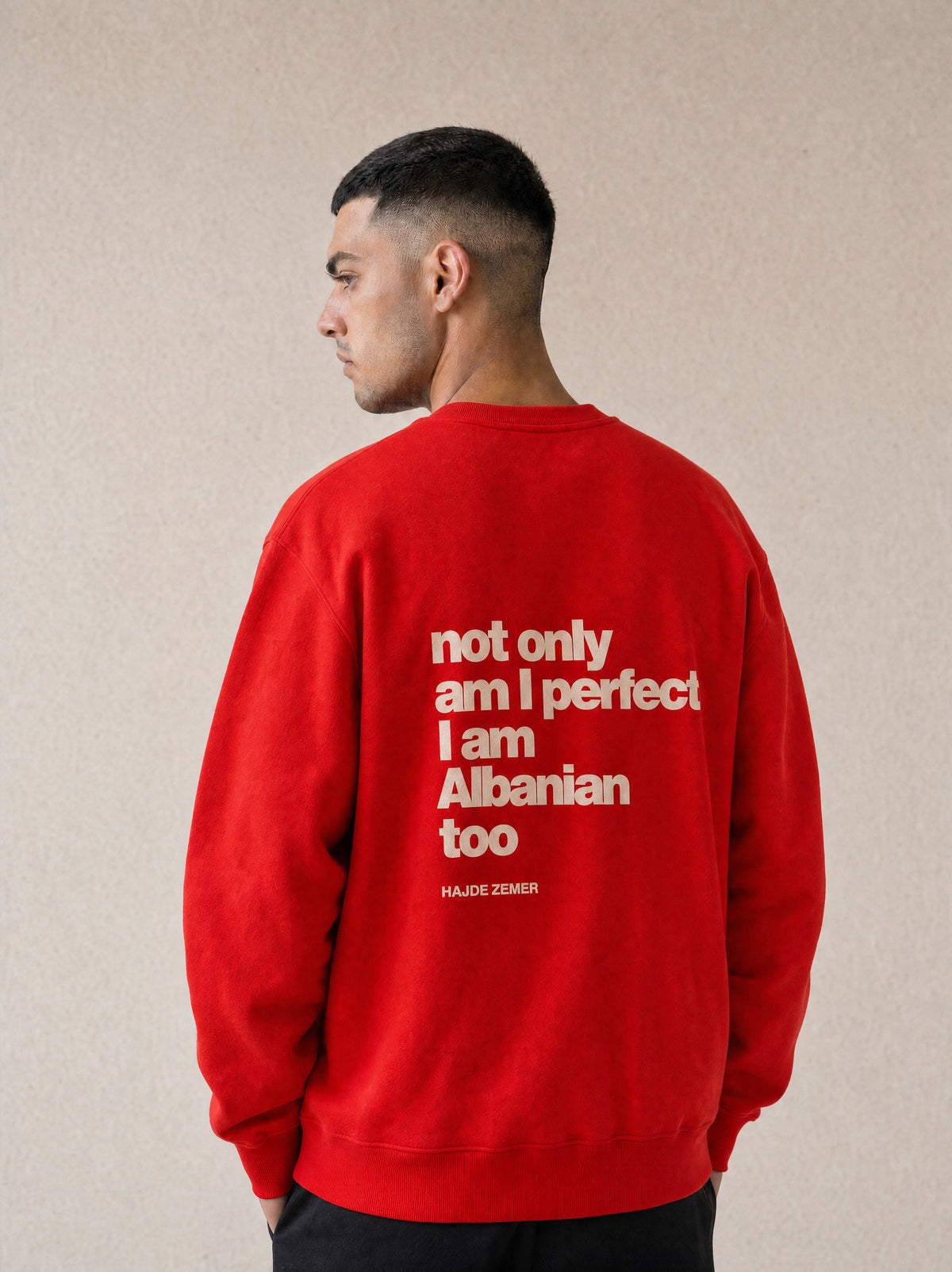 Man wearing the Hajde Zemer red crewneck, back view showing the printed text