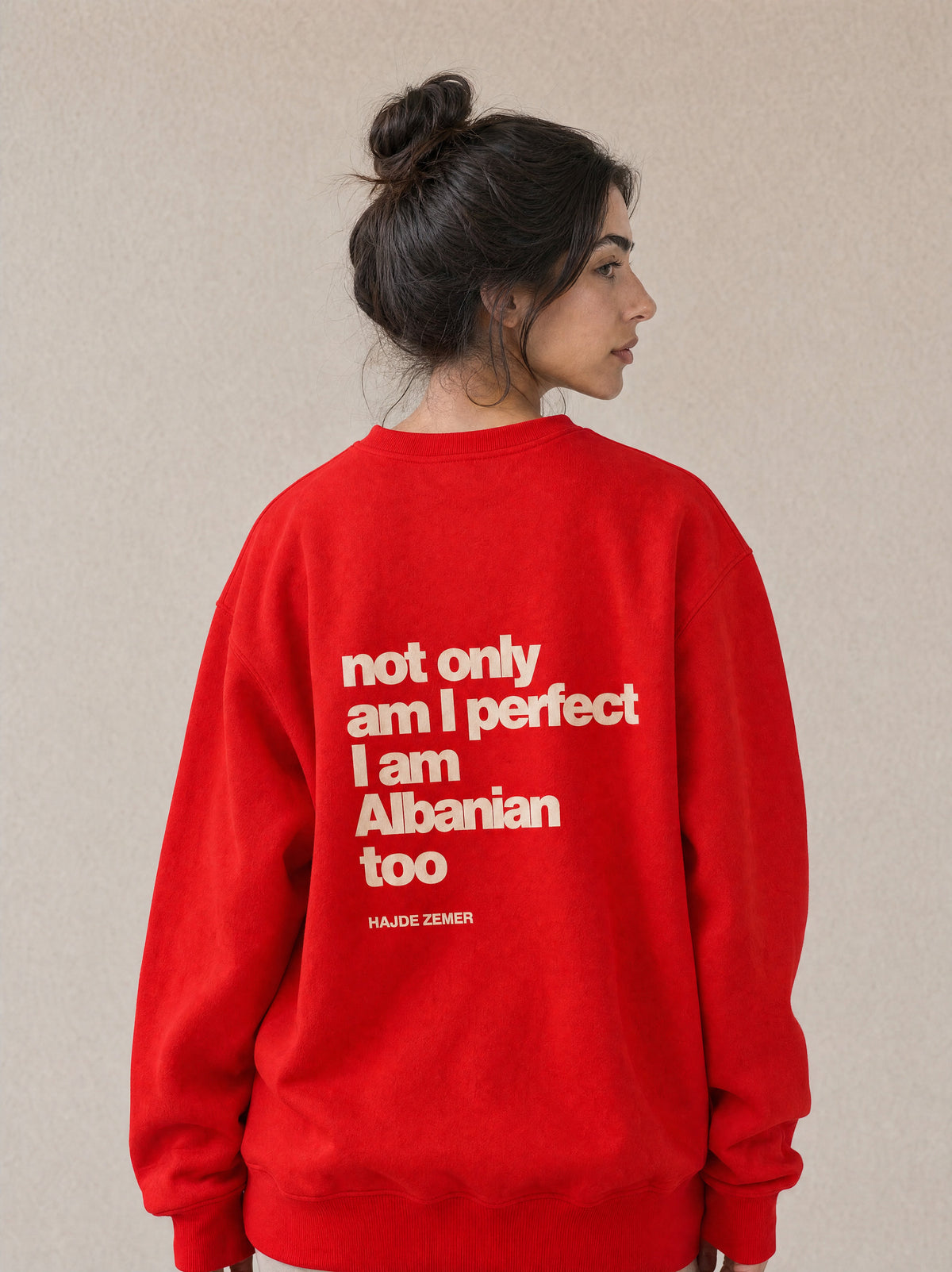 Woman wearing the Hajde Zemer red crewneck, back view showing the printed text