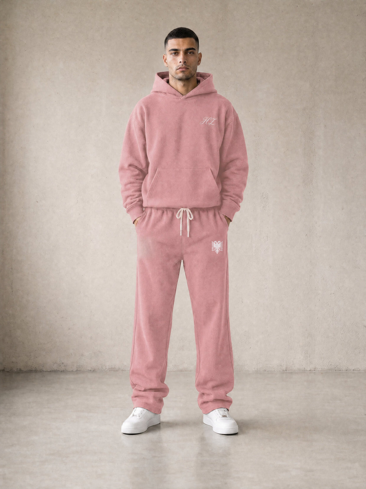 Design preview: Hajde Zemer HZ Essential Eagle Set in dusty rose pink, front view on a male model - cream HZ script on the chest, cream double-headed eagle at the sweatpant hip